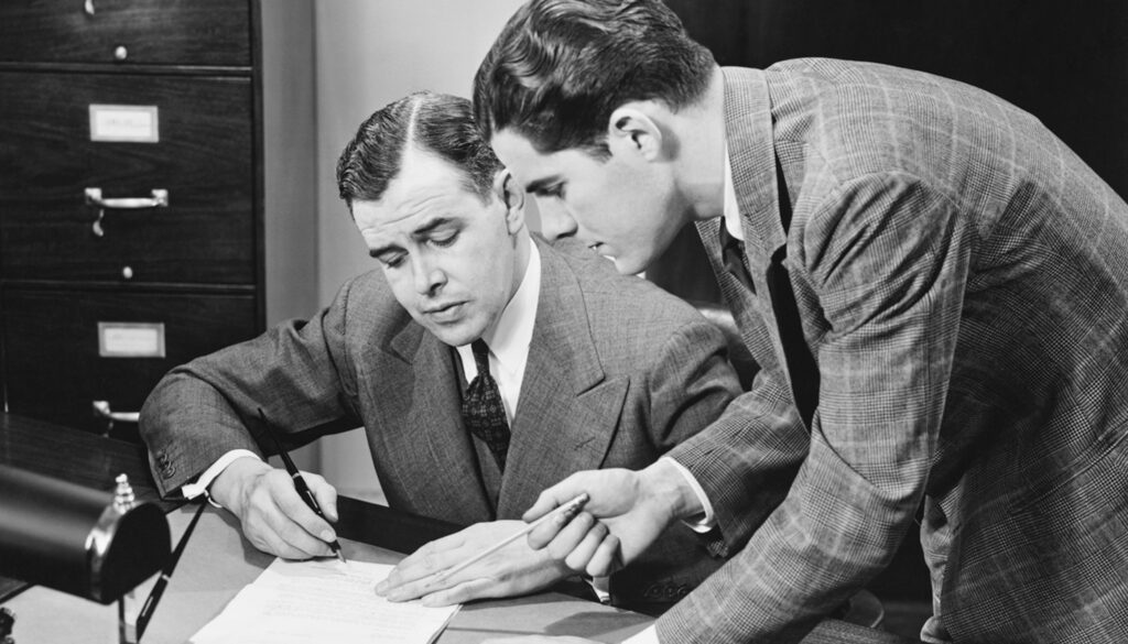 1950s black and white photo of two men collaborating on written content at a desk